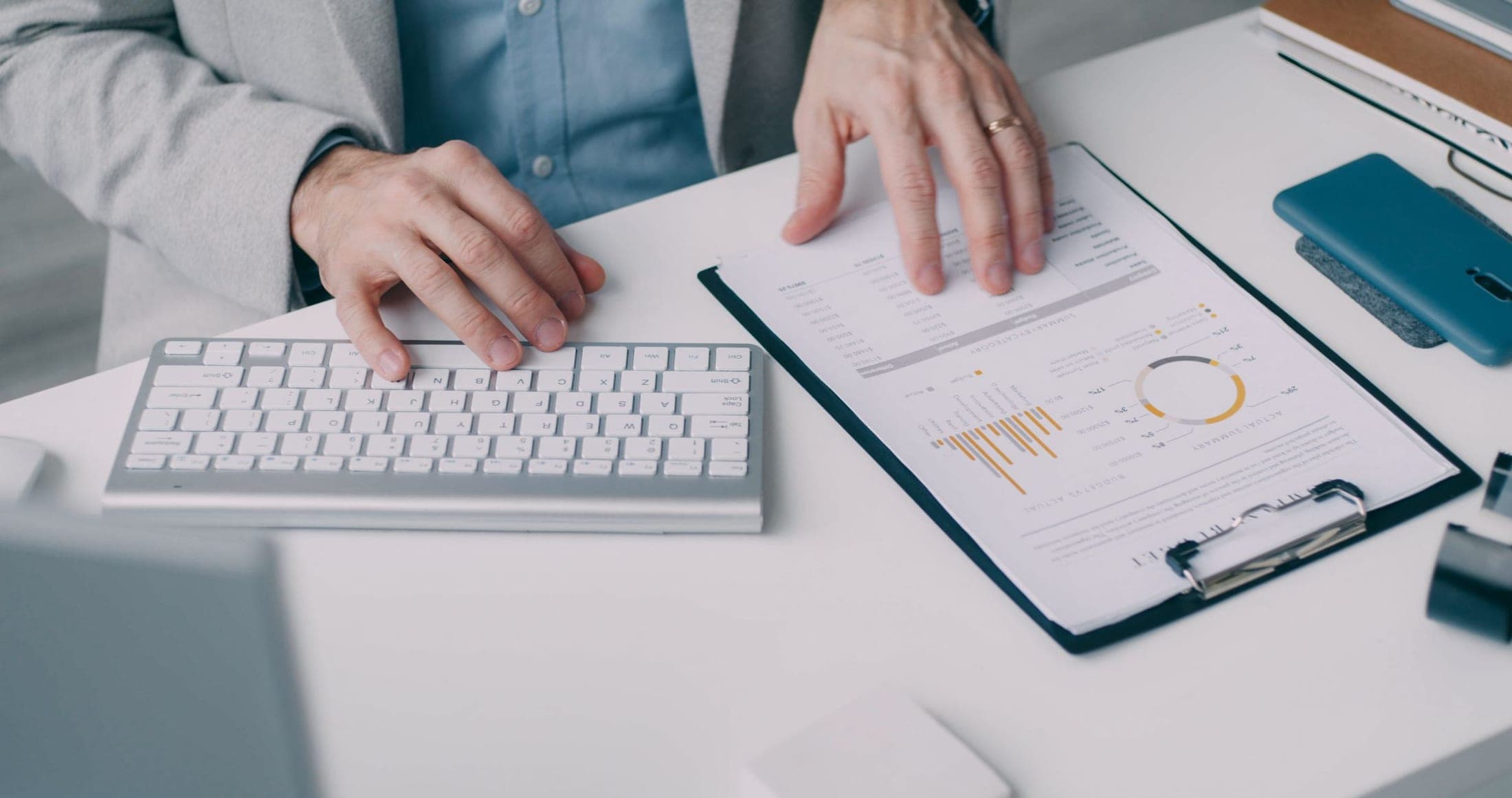 Hands reviewing a printed financial report beside a keyboard and clipboard
