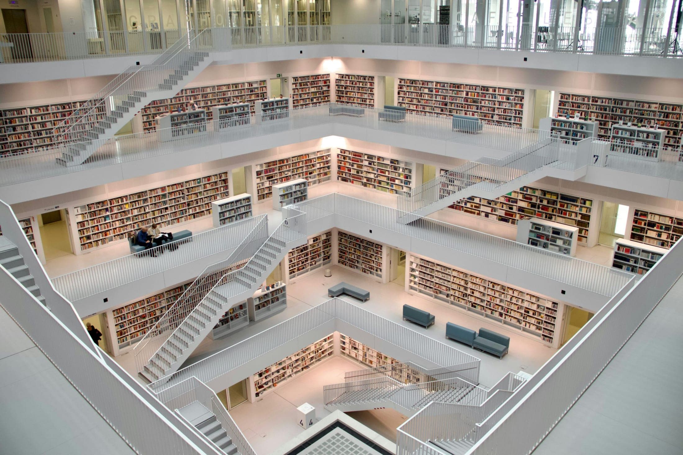 A white, multi-level library atrium with bookshelves and staircases