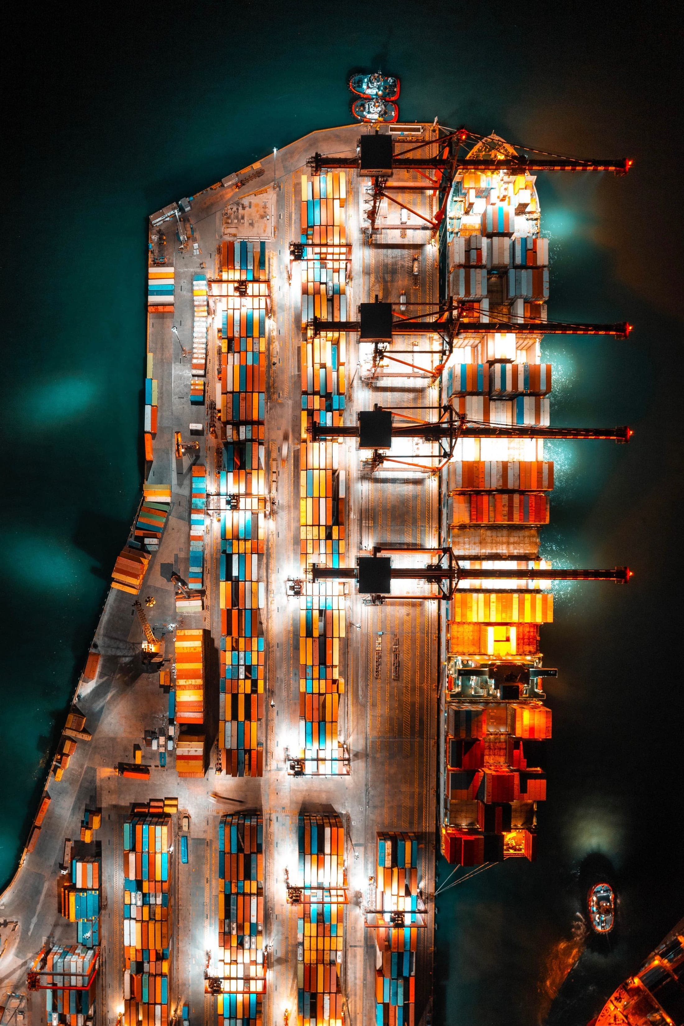 An aerial night view of a container terminal with stacked containers and lit cranes